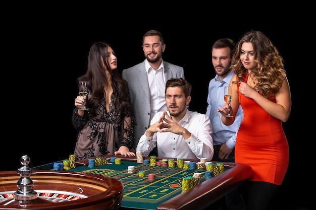 Foto gratuita gruppo di giovani che sembrano eccitati a girare la roulette. tavolo di roulette in un casinò. sfondio nero