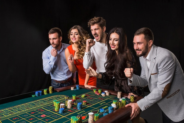 Free photo group of young people behind roulette table on black background. emotions players