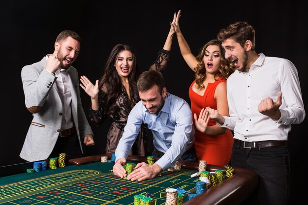 Group of young people behind roulette table on black background. Winning Player. Bright emotions