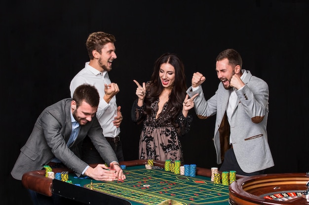 Group of young people behind roulette table on black background. The young man rejoices victory