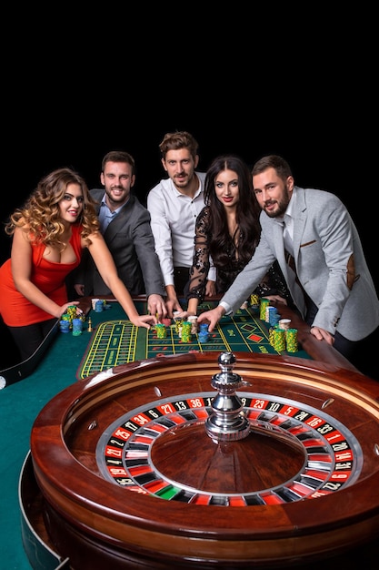 Free photo group of young people behind roulette table in a casino. black background