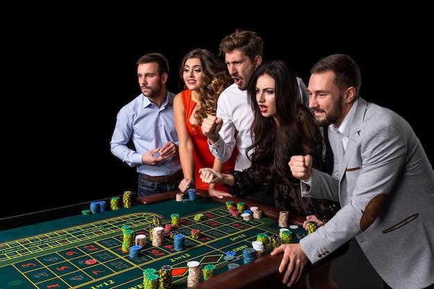 Free photo group of young people behind roulette table in a casino. black background