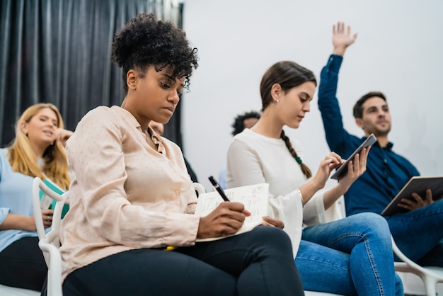 Group of young people sitting on conference together while raising their hands to ask a question. Business team meeting seminar training concept.