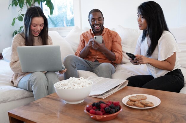 Group of young people using laptop together at home on sofa and having snacks