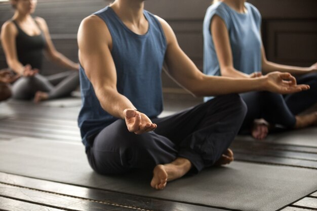 Group of young sporty people sitting in Sukhasana, close up