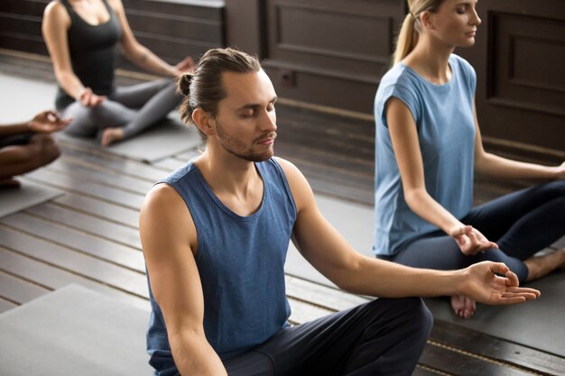 Group of young sporty people sitting in Sukhasana, close up