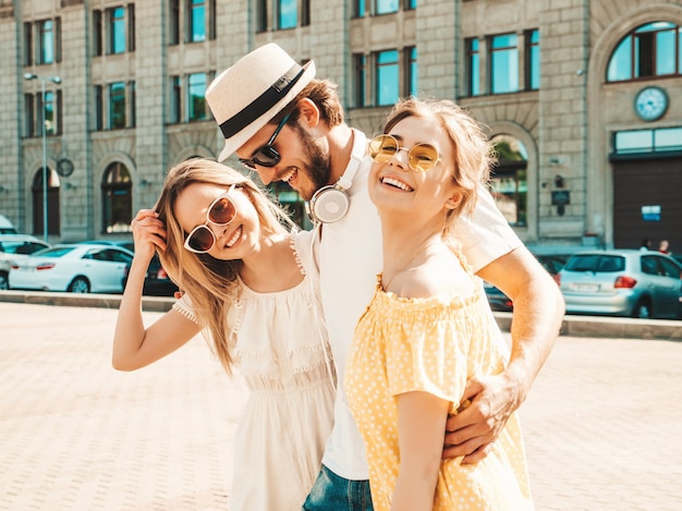 Group of young three stylish friends posing in the street. Fashion man and two cute girls dressed in casual summer clothes. Smiling models having fun in sunglasses.Cheerful women and guy going crazy