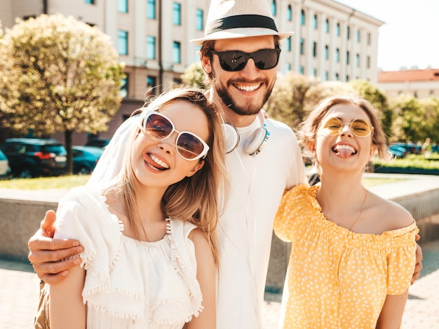 거리에서 포즈를 취하는 젊은 세 세련 된 친구의 그룹입니다. 패션 남자와 두 귀여운 여자 캐주얼 여름 옷을 입고. 선글라스에 재미 웃는 모델.