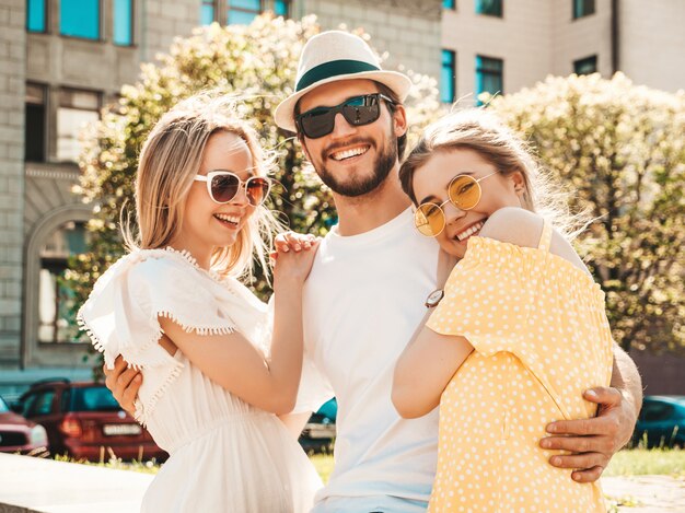 Group of young three stylish friends posing in the street. Fashion man and two cute girls dressed in casual summer clothes. Smiling models having fun in sunglasses.Cheerful women and guy going crazy