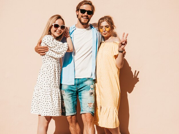 Group of young three stylish friends posing in the street. Fashion man and two cute girls dressed in casual summer clothes. Smiling models having fun in sunglasses.Cheerful women and guy going crazy