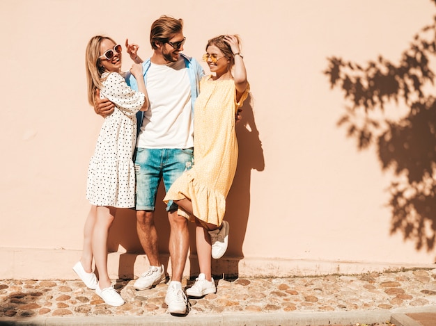 Free photo group of young three stylish friends posing in the street. fashion man and two cute girls dressed in casual summer clothes. smiling models having fun in sunglasses.cheerful women and guy going crazy