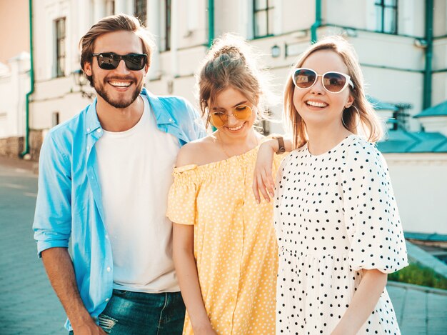 거리에서 포즈를 취하는 젊은 세 세련 된 친구의 그룹입니다. 패션 남자와 두 귀여운 여자 캐주얼 여름 옷을 입고. 선글라스에 재미 웃는 모델.