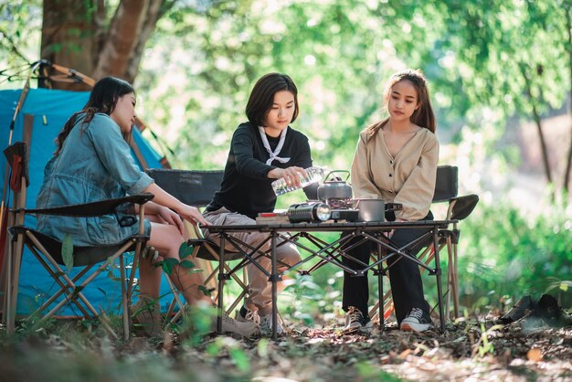 若い女性のグループは、公園のキャンプテントの前でガスストーブを使って鍋で食事を作るのを楽しんでいます