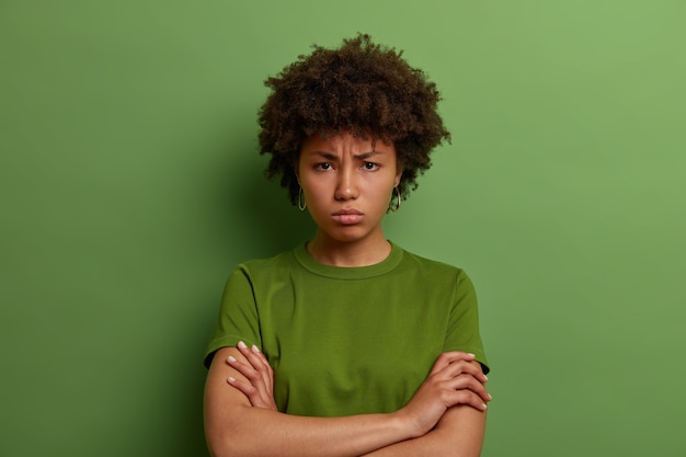 Free photo grumpy offended millennial woman holds hands crossed on chest, frowns face, has quarrel with someone, angry expression, wears green t shirt, being mad at you, feels insulted, unwilling to talk