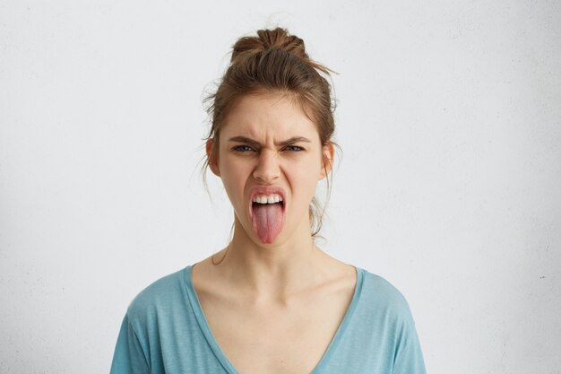 Сварливая женщина с узлом волос показывает язык, выражая отрицательные эмоции. Разъяренная женщина показывает свое отвращение во время ссоры