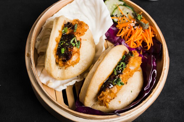 Gua bao steamed buns with salad inside the bamboo steamer on black background