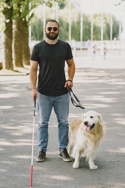 Guide dog helping blind man in the city. Handsome blind guy have rest with golden retriever in the city.
