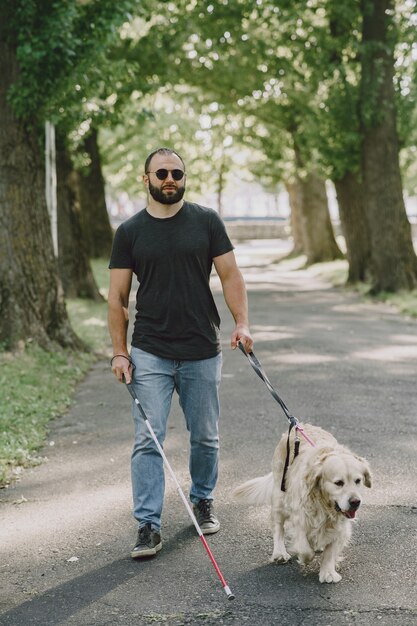 Guide dog helping blind man in the city. Handsome blind guy have rest with golden retriever in the city.