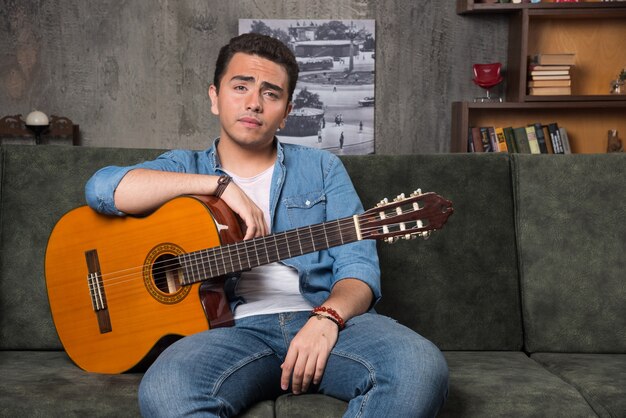 Guitar player holding a beautiful guitar and sitting on sofa. High quality photo