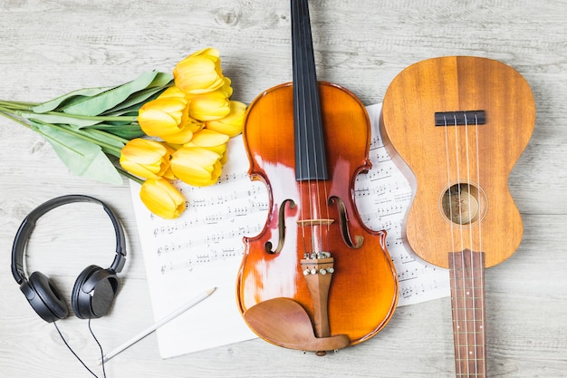 Foto gratuita chitarra; violino; tulipani; cuffie; matita sulla nota musicale sopra il tavolo