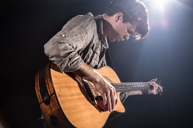 Гитарист, муз. Молодой человек играет на акустической гитаре на черном изолированном фоне. Остроконечный свет