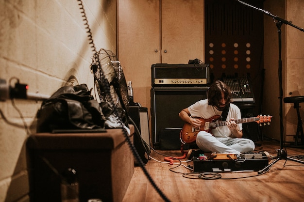 Гитарист, записывающий рок-музыку в студии, сидя на полу