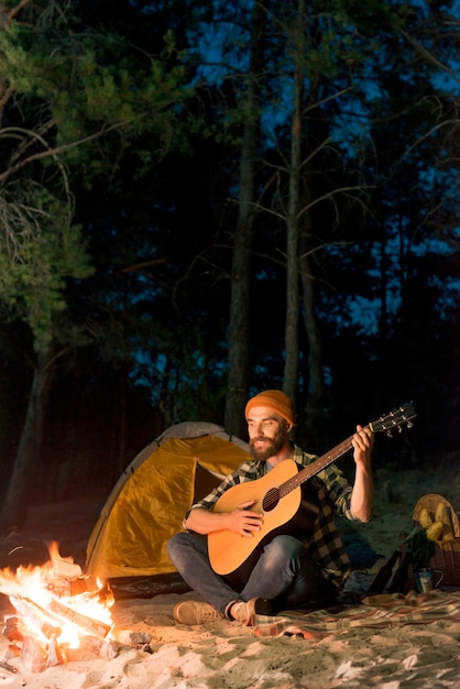 Guitarist singing at night by a tent with a campfire
