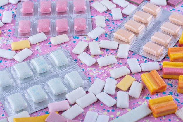 Gum tablet packs amid scattered bubblegum pieces on a colorful surface