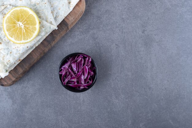 Gutab on the board next to a small bowl of grated red cabbage on the marble surface.