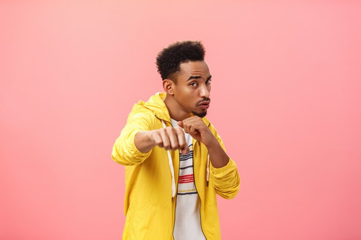 Free Photo guy acting cool bragging in front of girlfriend with mascules showing boxer moves standing in boxing pose with raised fist in punch gesture turning right as if fighting over pink background