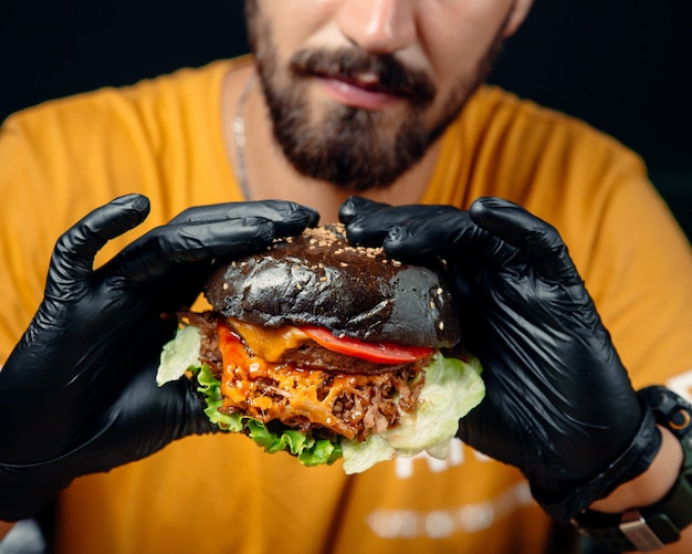 Guy in black gloves holds a juicy cheeseburger in brown bread