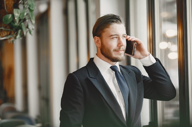 黒のスーツを着た男。携帯電話を持つ男性。オフィスのビジネスマン。