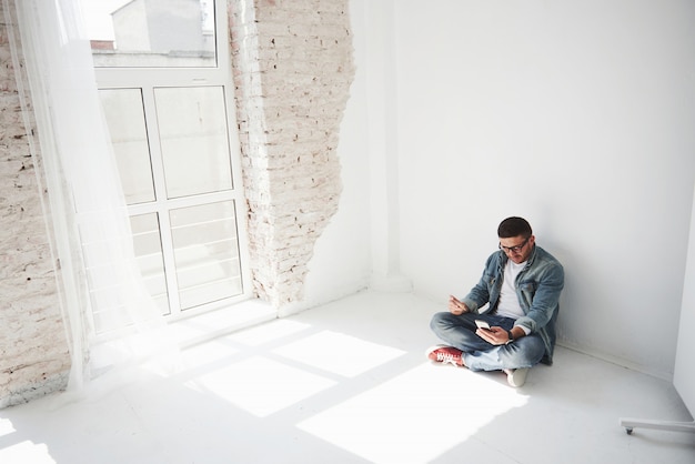 A guy in casual clothes is sitting at home in an empty apartment holding a credit card