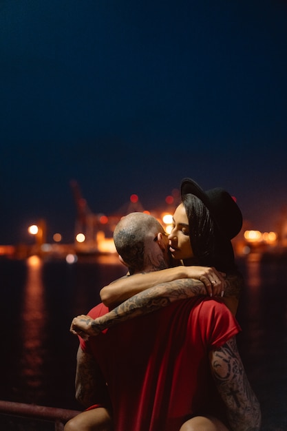 Free photo guy and girl hugging each other on a background of the night port