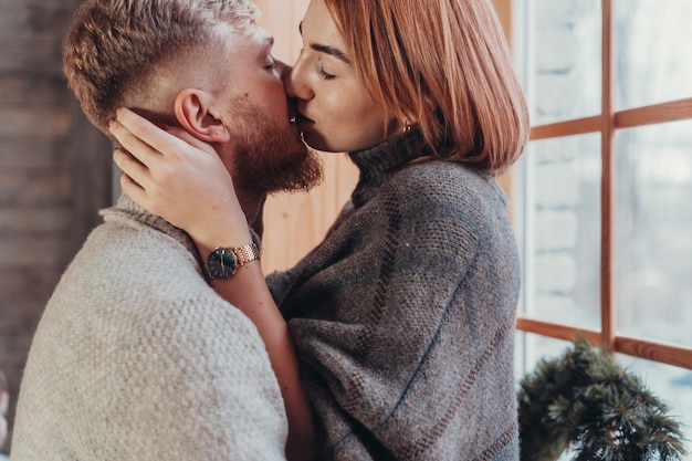 The guy and the girl kiss on the background of the window