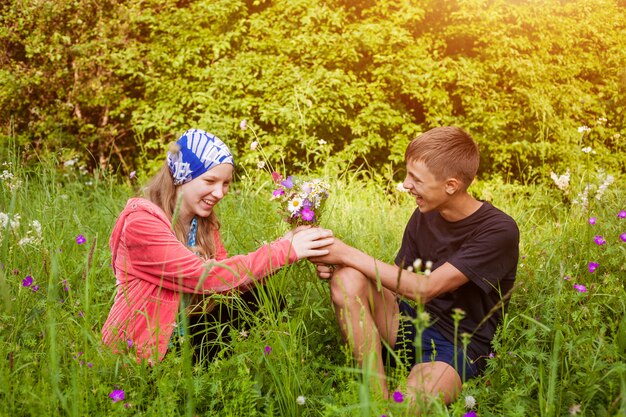 A guy gives a girl a bouquet of wild flowers sitting in a meadow