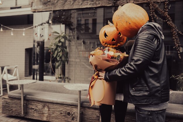 The guy gives his girlfriend a bouquet both with a pumpkin head