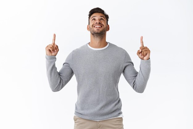 guy in grey sweater over t-shirt, raise head up and contemplate interesting product banner, pointing upwards intrigued