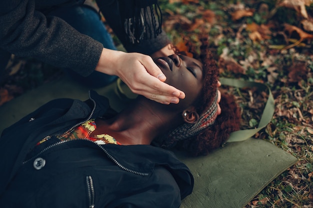 Guy help a woman. Afro girl is lying unconscious. Providing first aid in the park