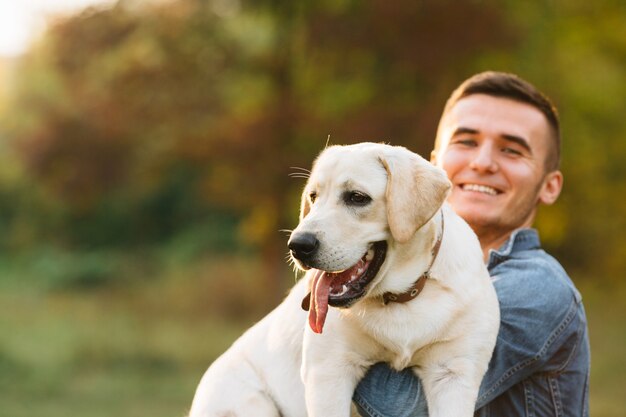 Guy holding his friend dog labrador and smiling at sunset