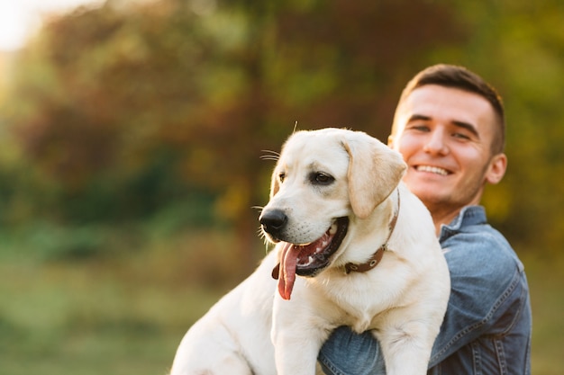 Guy holding his friend dog labrador and smiling at sunset