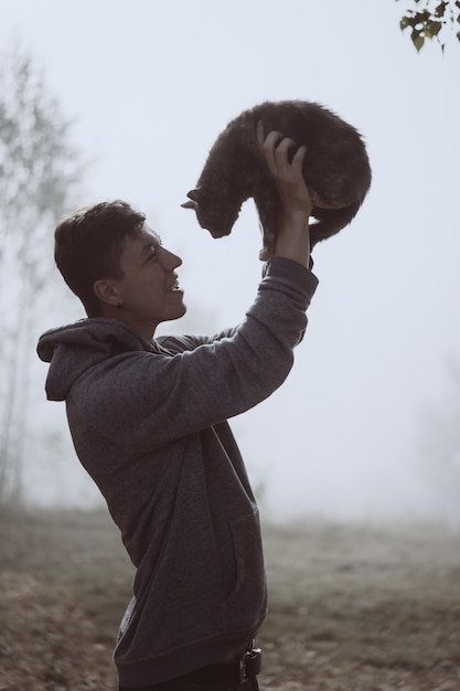 The guy holds a cat in the park. The park is shrouded in fog