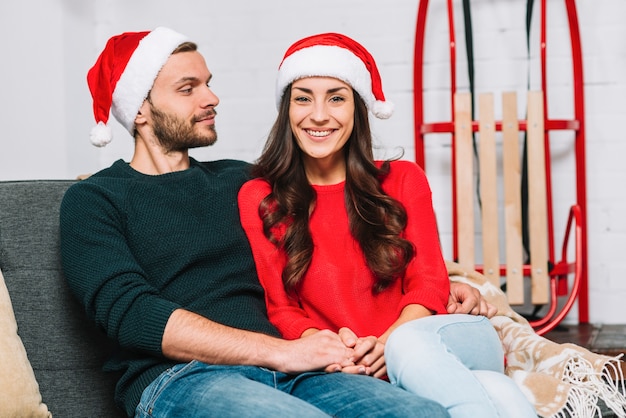 Free photo guy and lady in party hats hugging on sofa