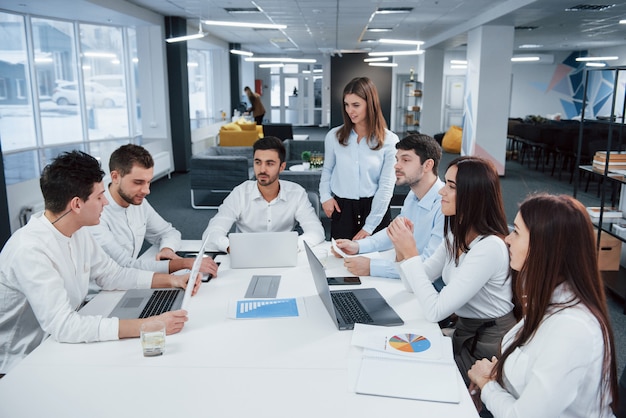 Guy on the left side talking and colleagues is listening to him. Group of young freelancers in the office have conversation and smiling