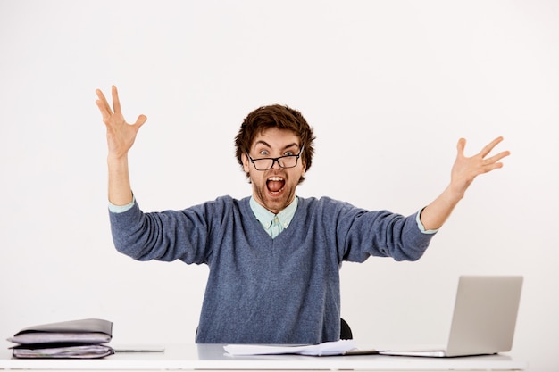 Guy losing temper at job, sit office desk with laptop and piles documents, raising hands dismay, scream annoyed and distressed