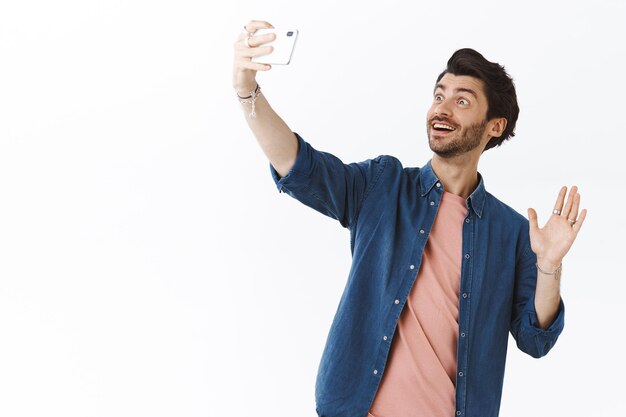 Guy making vlog during travelling abroad, saying hello to followers as record video on smartphone, raise mobile phone high to get right angle and take shot, waving hand at camera