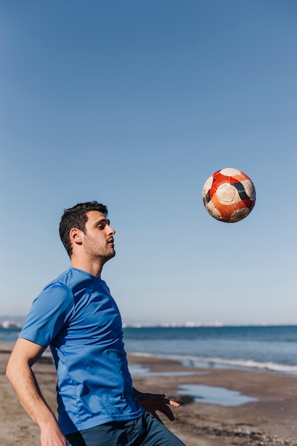 Free photo guy playing football at the beach