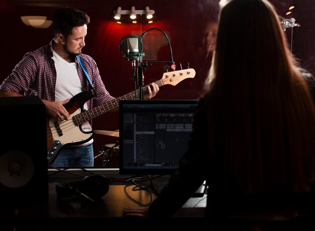 Guy playing guitar and woman recording from behind view