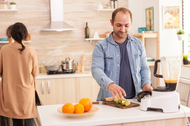 Guy preparing tasty smoothie in kitchen using blender. Healthy carefree and cheerful lifestyle, eating diet and preparing breakfast in cozy sunny morning