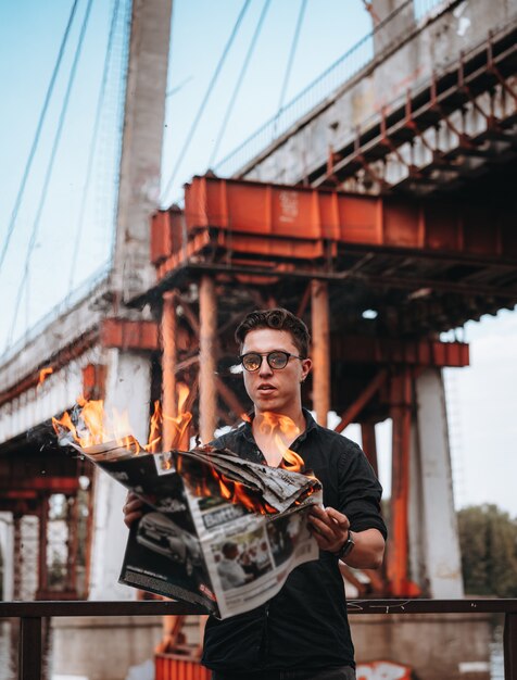 Парень читает горящую газету перед мостом